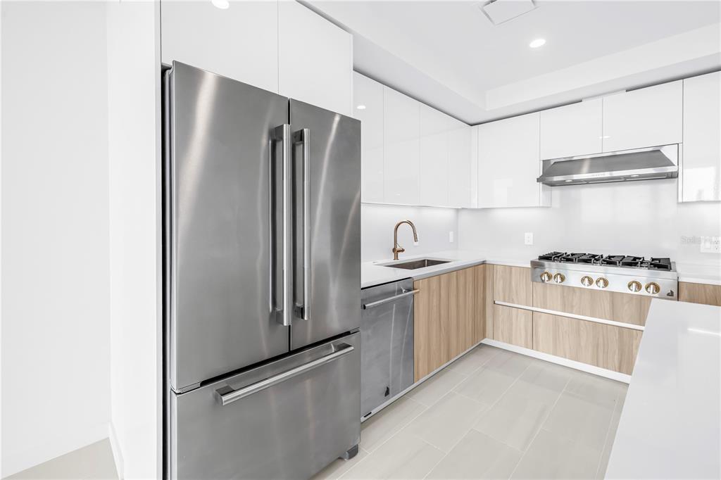 A modern kitchen features white upper cabinets, wood-tone lower cabinets, stainless steel appliances, and tile flooring — 400 CENTRAL AVENUE UNIT 1608, ST PETERSBURG, FL