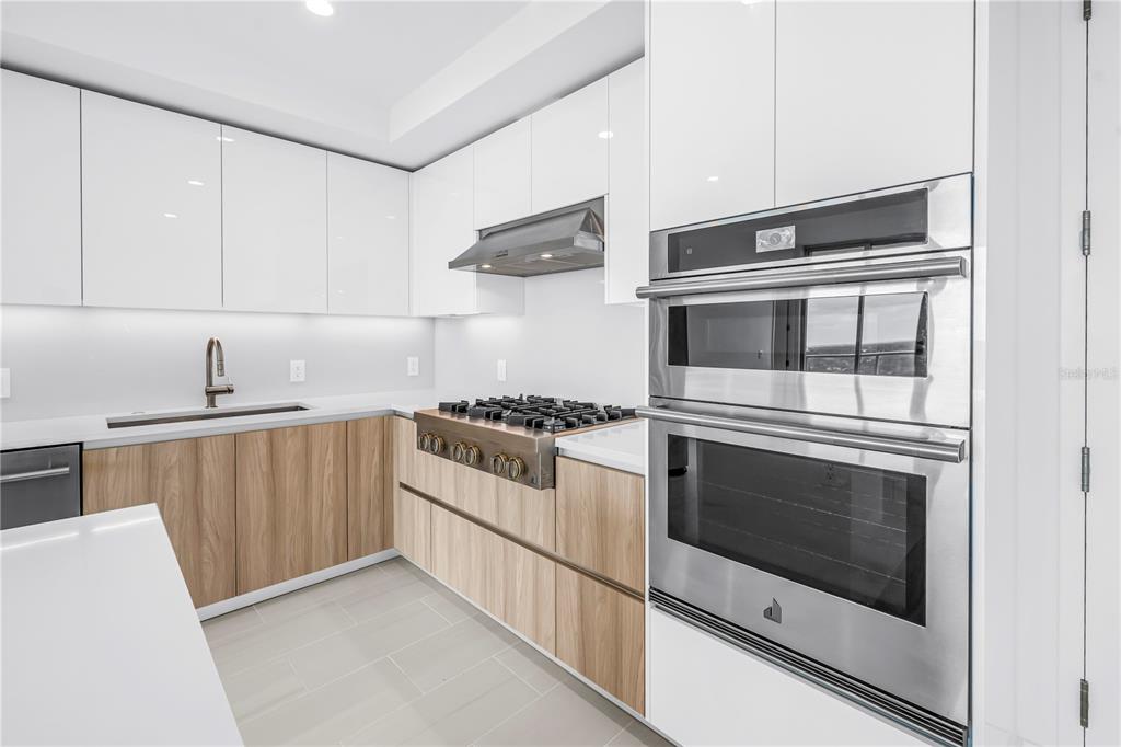 A modern kitchen features white glossy upper cabinets, wood-grain lower cabinets, and stainless steel appliances — 400 CENTRAL AVENUE UNIT 1608, ST PETERSBURG, FL