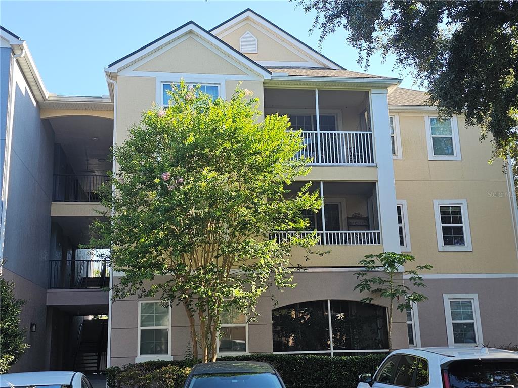 A three-story apartment building exterior features tan stucco walls, screened balconies, and a central tree — 3446 SOHO STREET UNIT 108, ORLANDO, FL