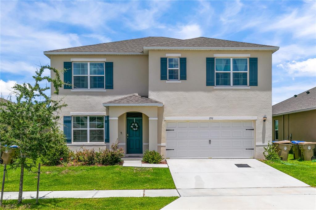 A two-story suburban house with a beige stucco exterior, teal shutters, and a two-car garage — 1591 BARBERRY DRIVE, KISSIMMEE, FL