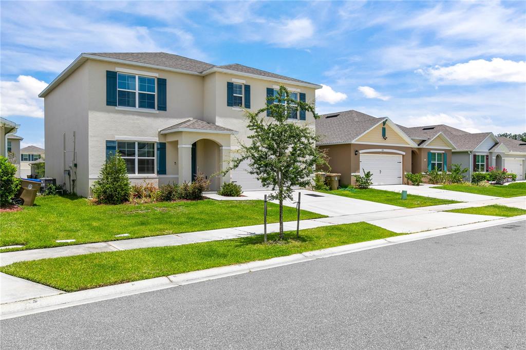 A two-story suburban house with blue shutters and a paved driveway under a blue sky — 1591 BARBERRY DRIVE, KISSIMMEE, FL