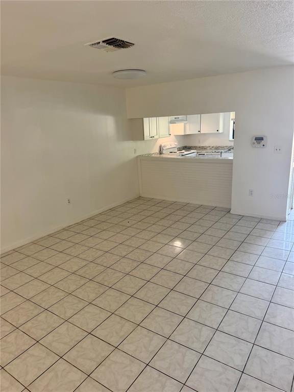 An open-concept room features white walls, light-colored floor tiles, and a kitchen pass-through window — 1549 TANGELO CIRCLE, KISSIMMEE, FL