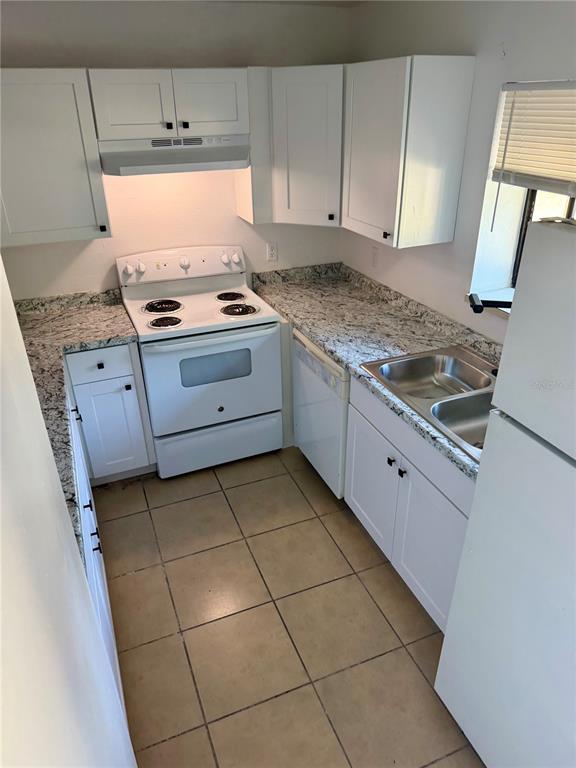 A small kitchen features white cabinets, granite countertops, a white stove, and tiled flooring — 1549 TANGELO CIRCLE, KISSIMMEE, FL