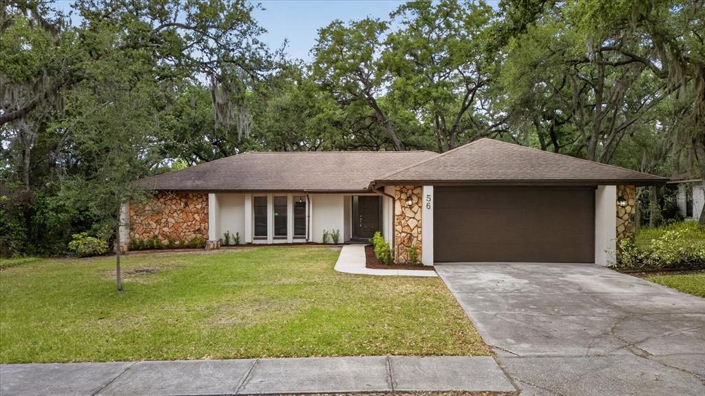 A single-story house features a stone facade, a brown garage door, and a grassy yard — 56 BAY WOODS DRIVE, SAFETY HARBOR, FL