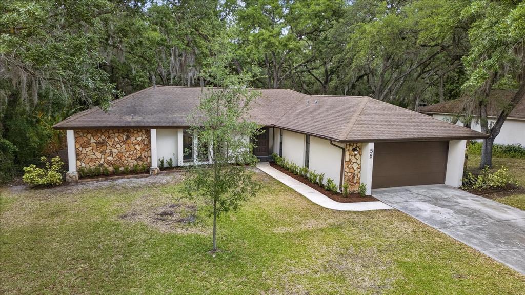 A single-story house with a stone facade, brown roof, and attached garage sits on grass — 56 BAY WOODS DRIVE, SAFETY HARBOR, FL