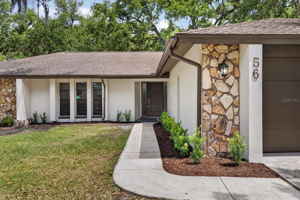 A single-story house exterior features a stone facade, a brown garage door, and a walkway — 56 BAY WOODS DRIVE, SAFETY HARBOR, FL