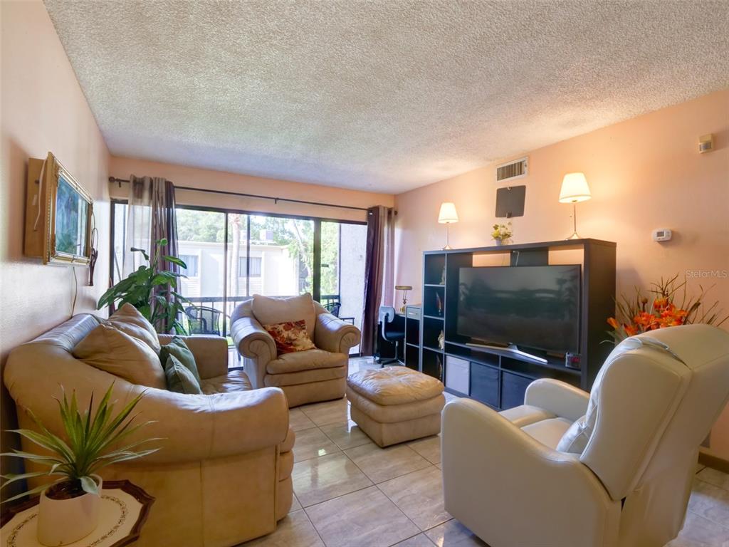 A living room features beige leather furniture, tile flooring, and a large television entertainment center — 3242 S SEMORAN BOULEVARD UNIT 22, ORLANDO, FL