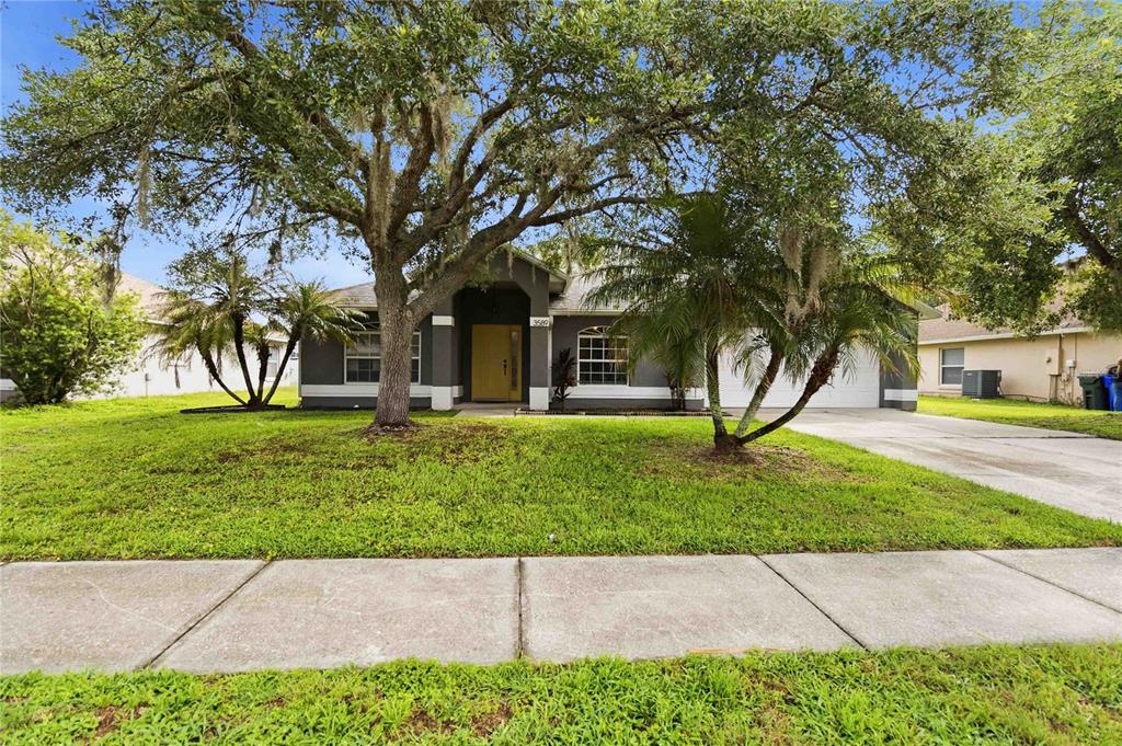 A single-story house with a yellow front door, gray exterior, and large shade trees — 3589 YELLOW BIRD COURT, ST CLOUD, FL