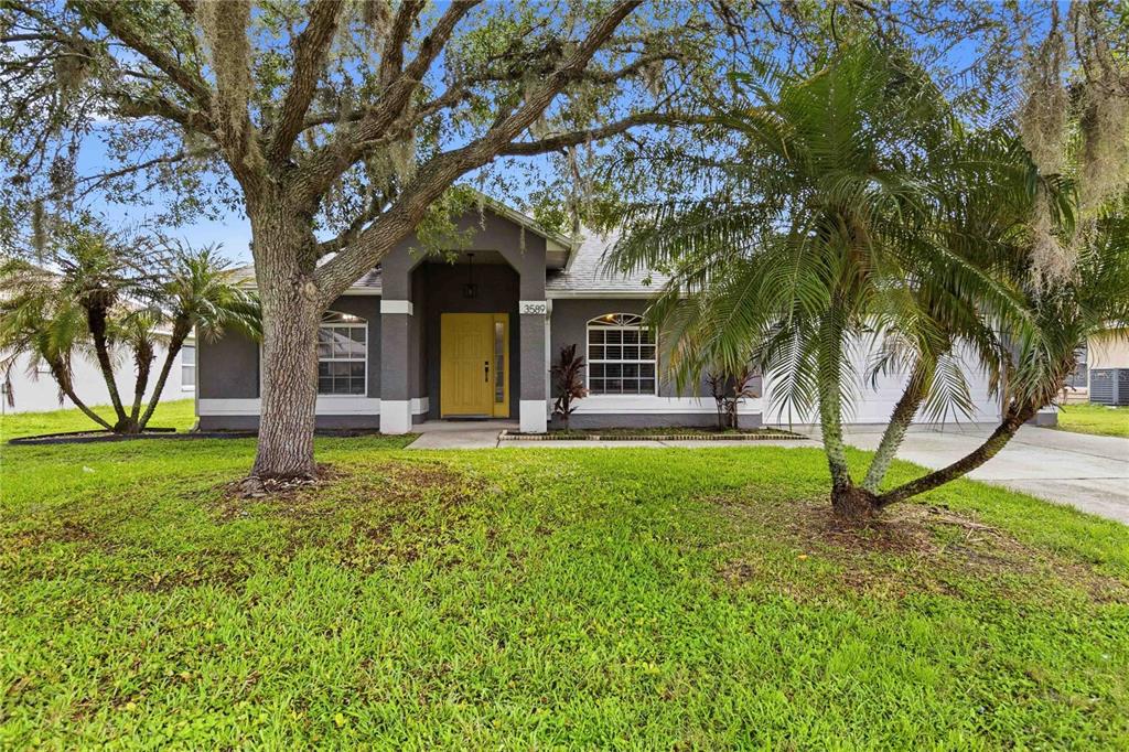 A single-story gray house with a yellow front door and a large tree in front — 3589 YELLOW BIRD COURT, ST CLOUD, FL