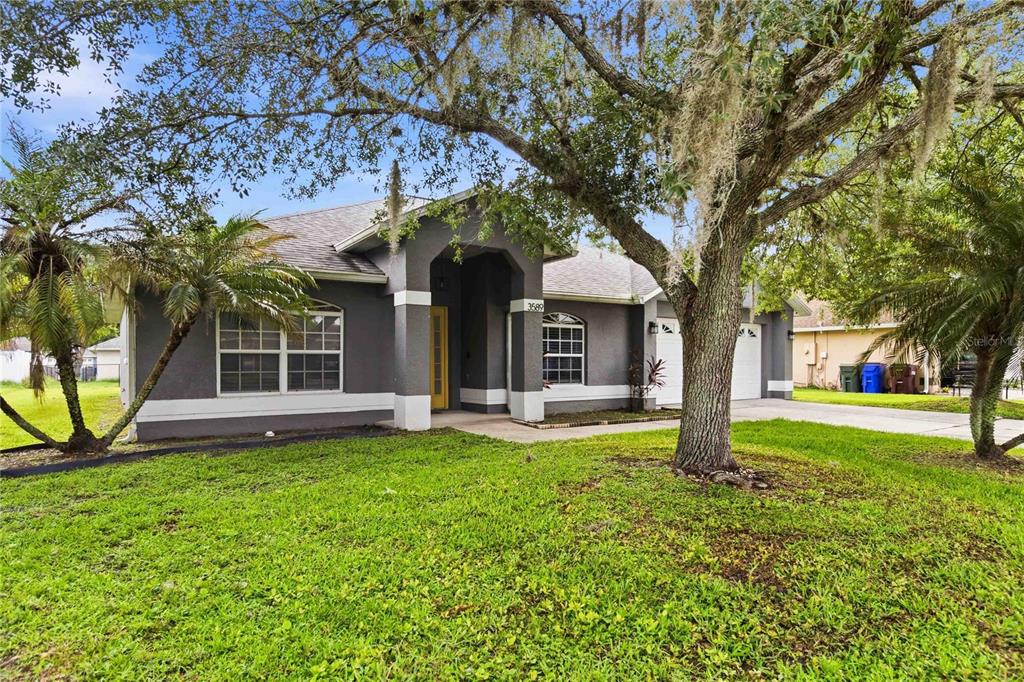 A gray single-story house with a yellow front door and a large oak tree — 3589 YELLOW BIRD COURT, ST CLOUD, FL
