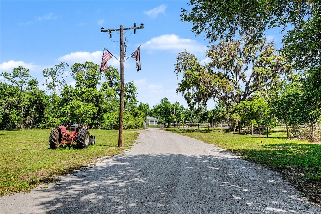 A gravel driveway leads toward a house past a red tractor and utility pole — 15750 WILSON ROAD, SARASOTA, FL