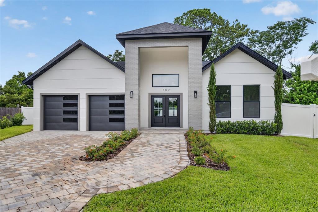 A modern single-story house with a brick entryway, two garage doors, and a paved walkway — 102 BELL PLACE, WINTER PARK, FL