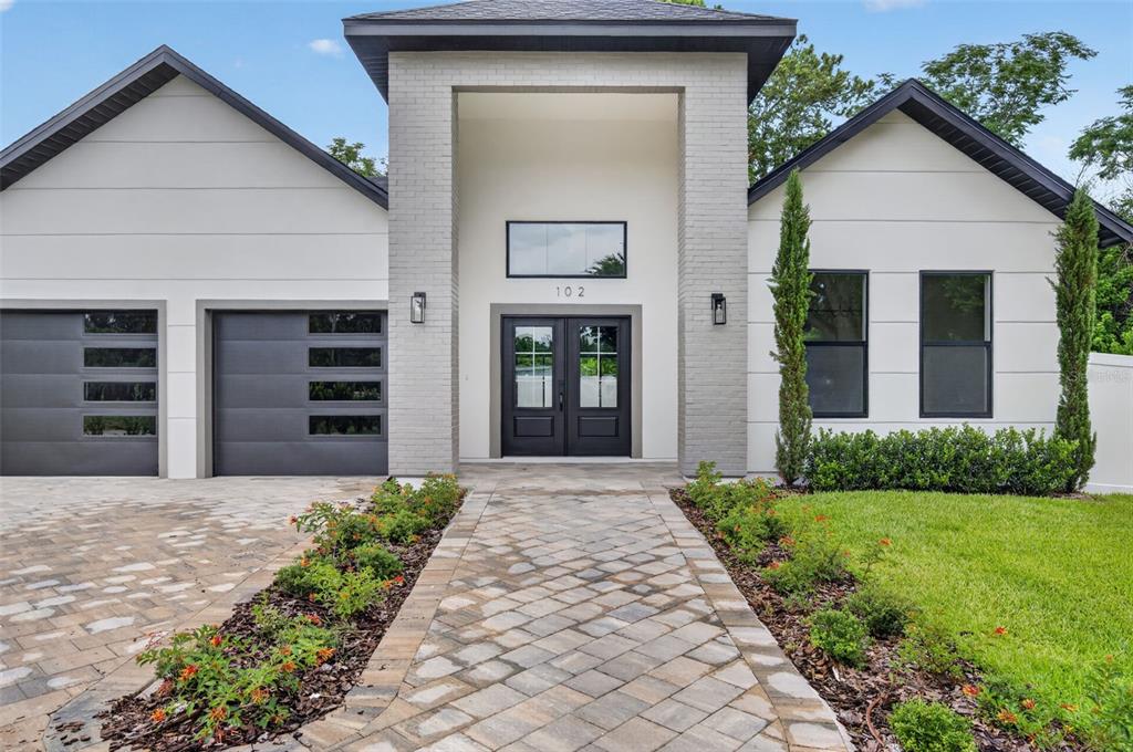 A modern house exterior features a brick entryway, double front doors, and a paved walkway — 102 BELL PLACE, WINTER PARK, FL