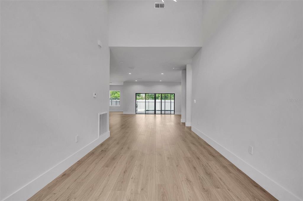 A bright, empty room with high ceilings, light wood-look flooring, and large sliding glass doors — 102 BELL PLACE, WINTER PARK, FL