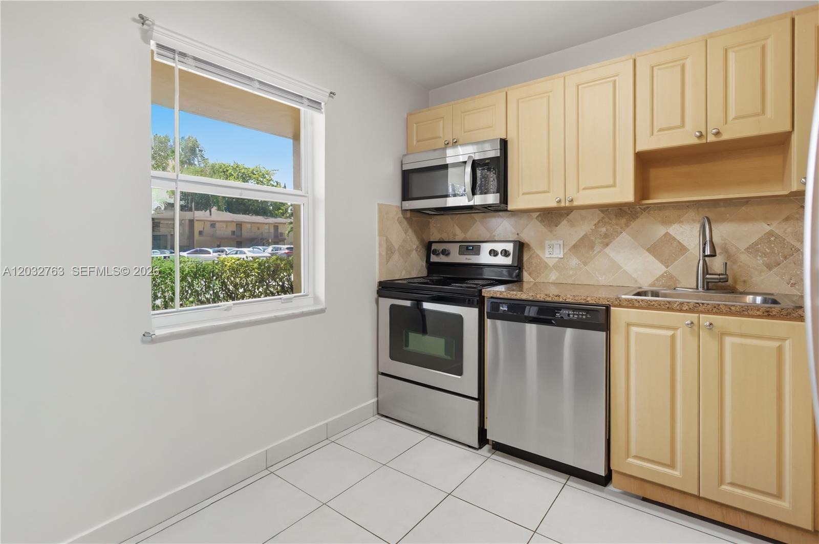 A kitchen features light wood cabinets, stainless steel appliances, tile flooring, and a window view — 251 NW 76th Ave # 106, Margate FL 33063, MARGATE, FL