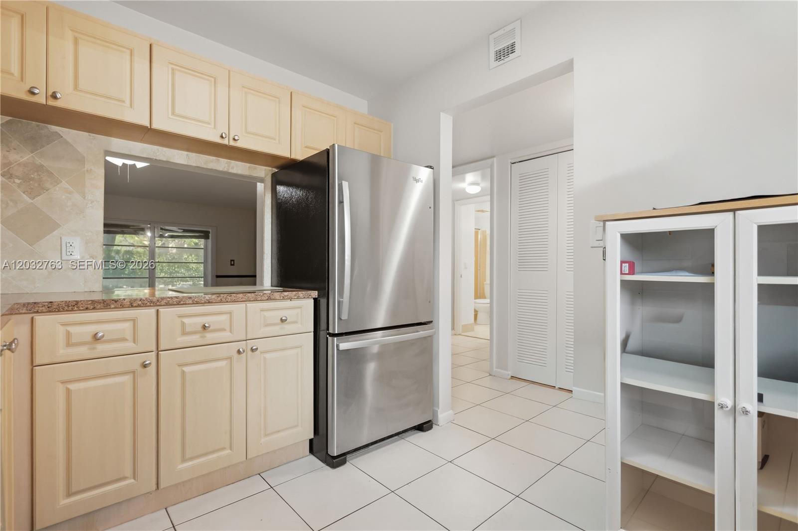 A kitchen features light wood cabinets, stainless steel appliances, and white tile flooring — 251 NW 76th Ave # 106, Margate FL 33063, MARGATE, FL