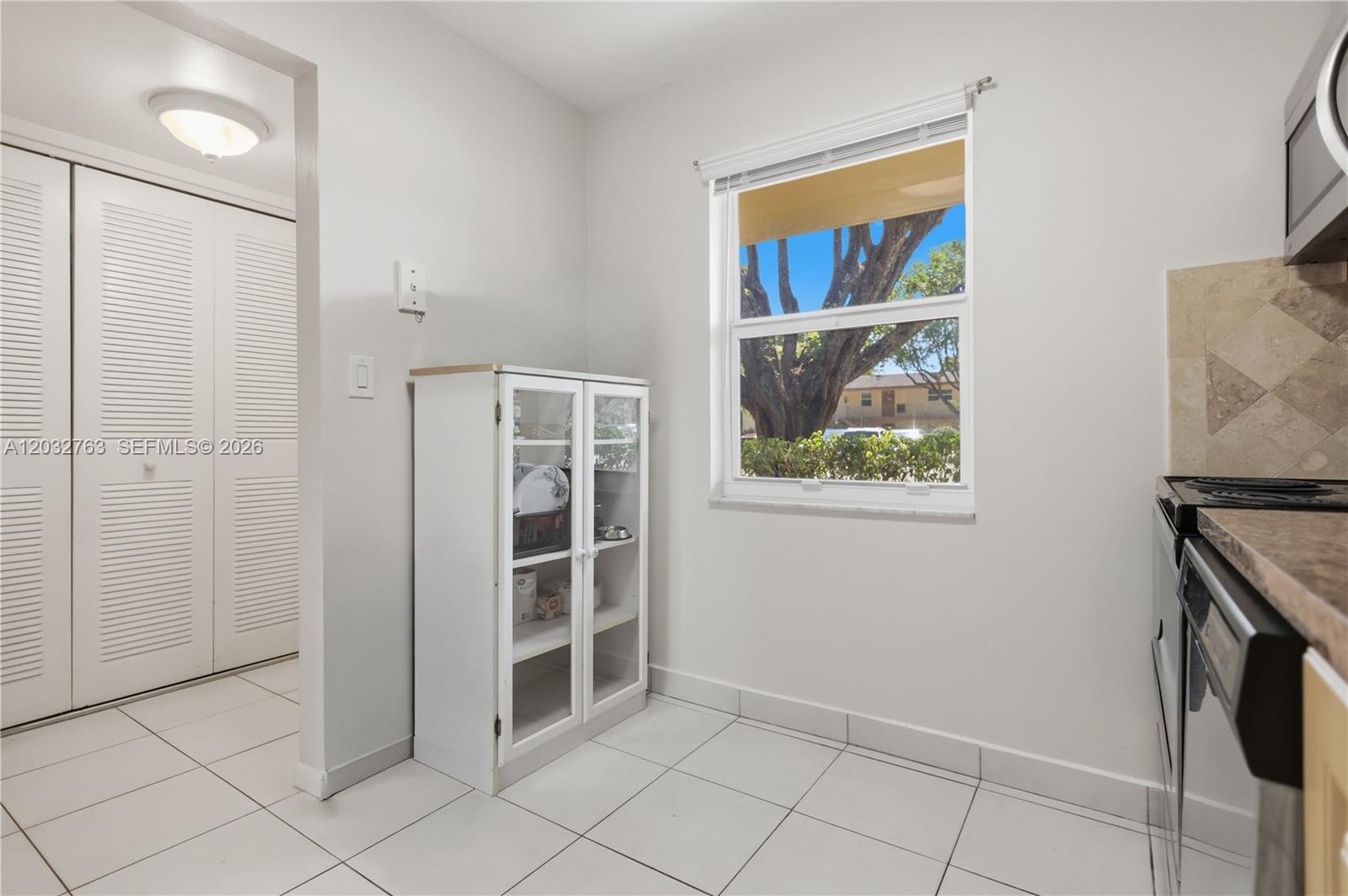 A kitchen area features white tile flooring, a glass-front cabinet, and a window with outdoor views — 251 NW 76th Ave # 106, Margate FL 33063, MARGATE, FL