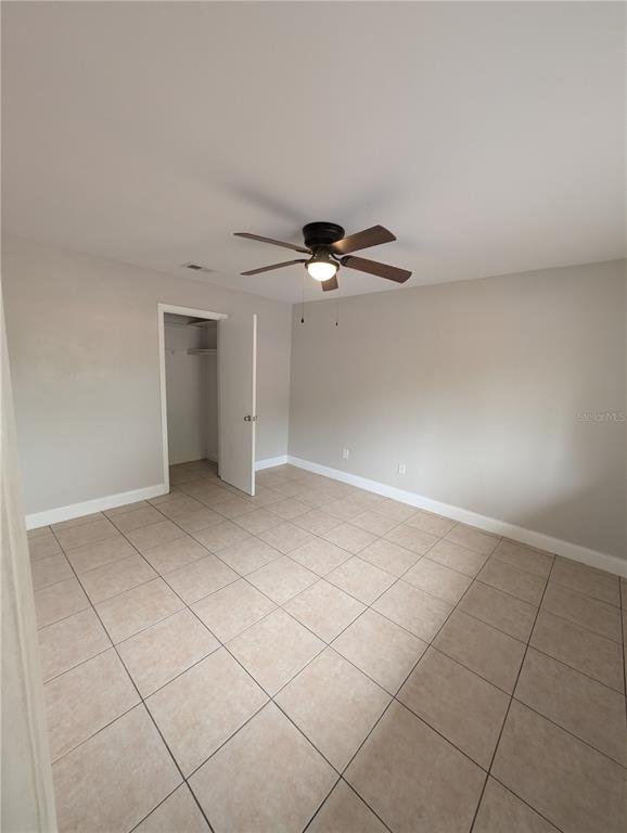 An empty bedroom features light gray walls, a ceiling fan, and beige tiled flooring — 803 NW 40TH AVENUE, GAINESVILLE, FL