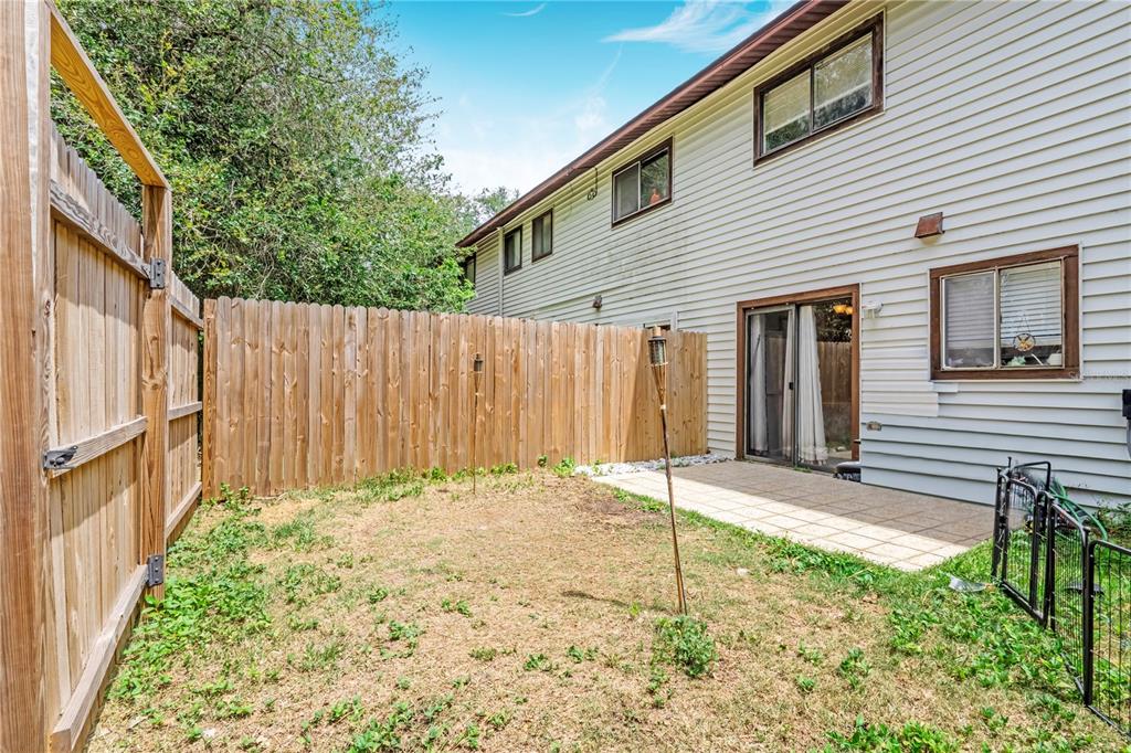 A fenced backyard features a small concrete patio and a two-story house with siding — 322 CANAL ROAD UNIT D22, EDGEWATER, FL