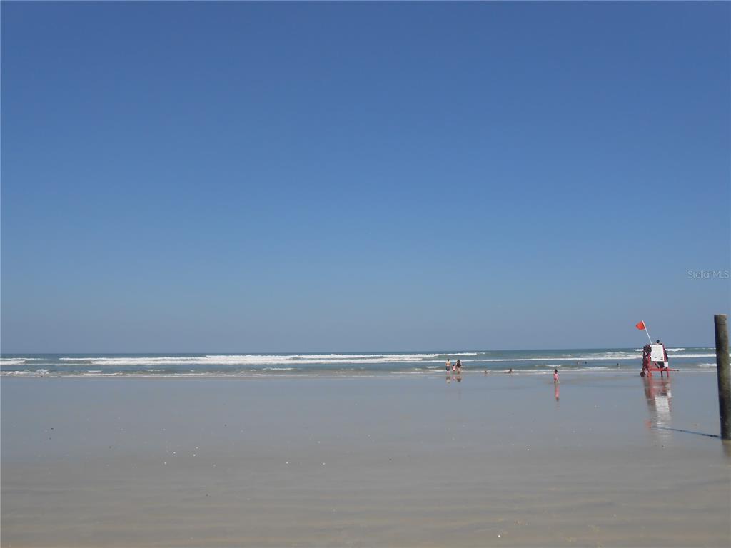 A wide, sandy beach features a lifeguard stand with a red flag near the ocean — 322 CANAL ROAD UNIT D22, EDGEWATER, FL