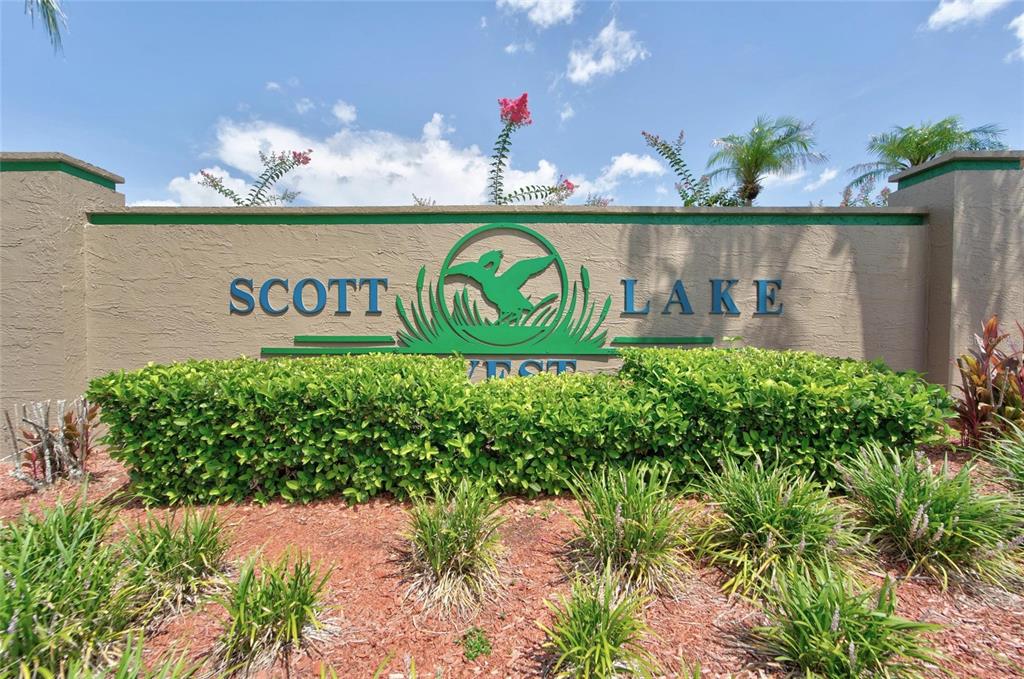 A beige stucco sign for Scott Lake West stands behind a manicured hedge and landscaping — 692 JESSANDA CIRCLE, LAKELAND, FL