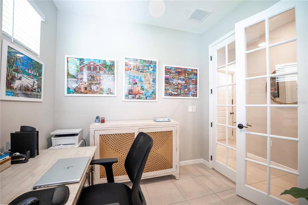 A home office features a desk, a cane-front cabinet, wall art, and glass-paneled French doors — 8764 SW 58TH STREET ROAD, OCALA, FL