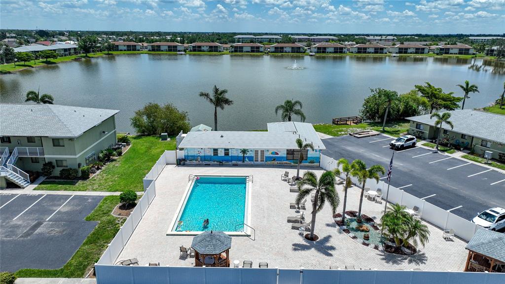 An aerial view shows a swimming pool, a clubhouse, and a lake with a fountain — 25225 RAMPART BOULEVARD UNIT 1607, PUNTA GORDA, FL