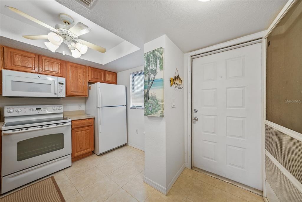 A kitchen with wood cabinets, white appliances, tile flooring, and a ceiling fan — 25225 RAMPART BOULEVARD UNIT 1607, PUNTA GORDA, FL