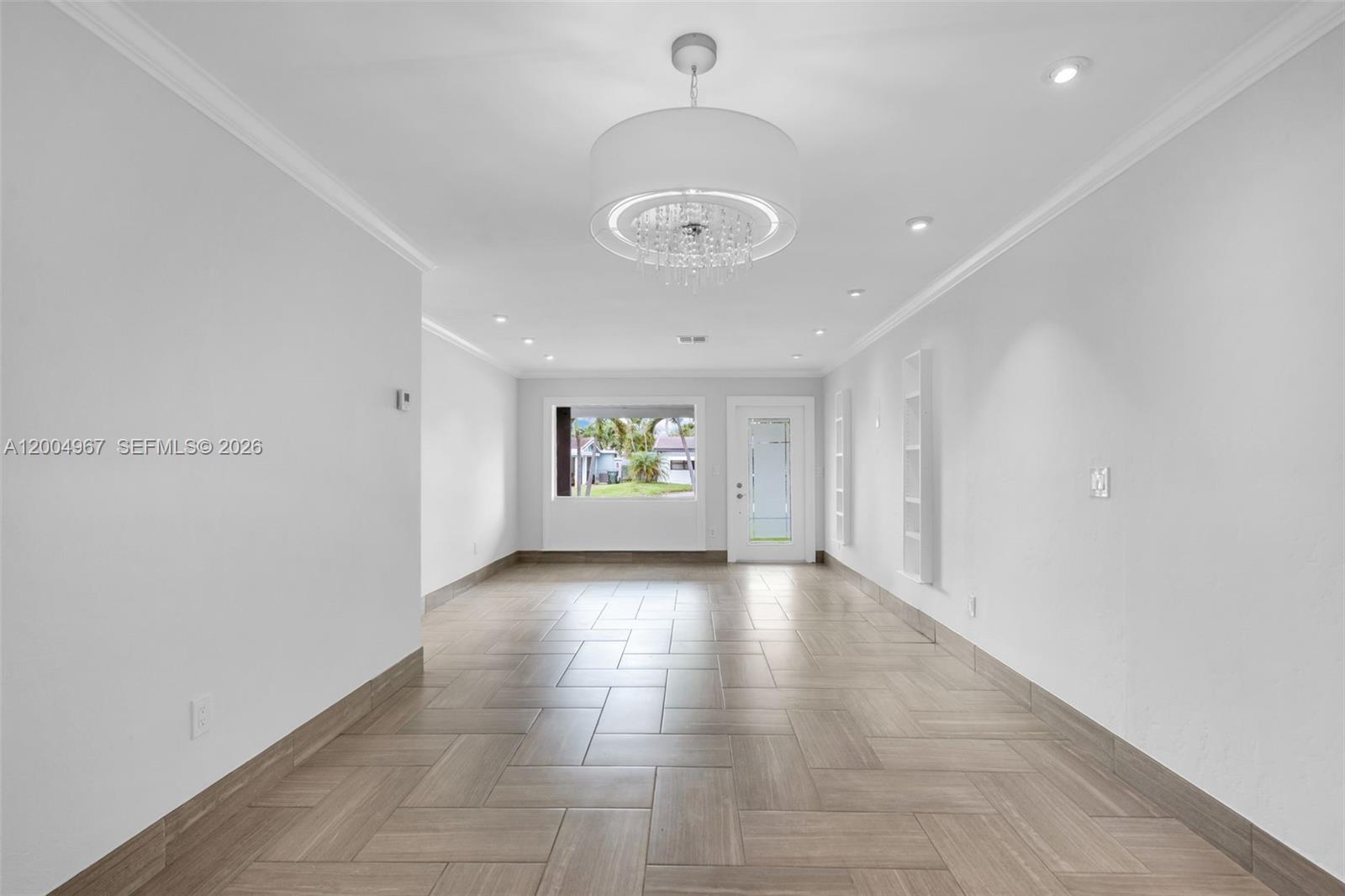 An empty room features light-colored tile flooring, a modern drum chandelier, and a front door — OAKLAND PARK, FL
