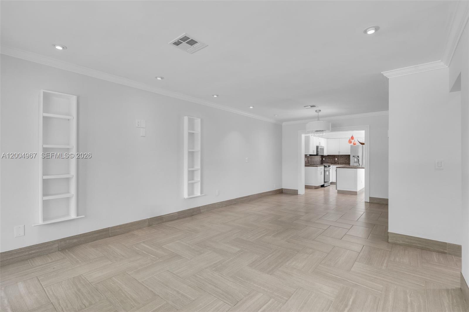 An empty living room with light-colored tile flooring leads into a kitchen — OAKLAND PARK, FL