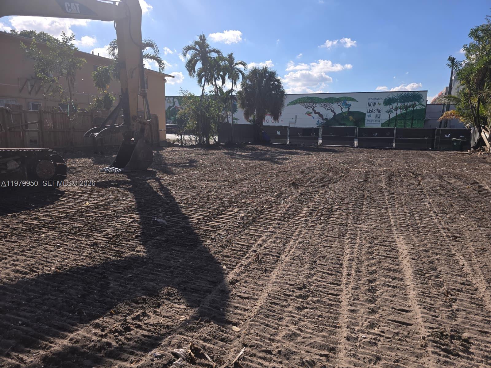 A construction excavator sits on a cleared, dirt-covered lot with palm trees in the background — 951 NW 37th Ave, Miami FL 33125, MIAMI, FL