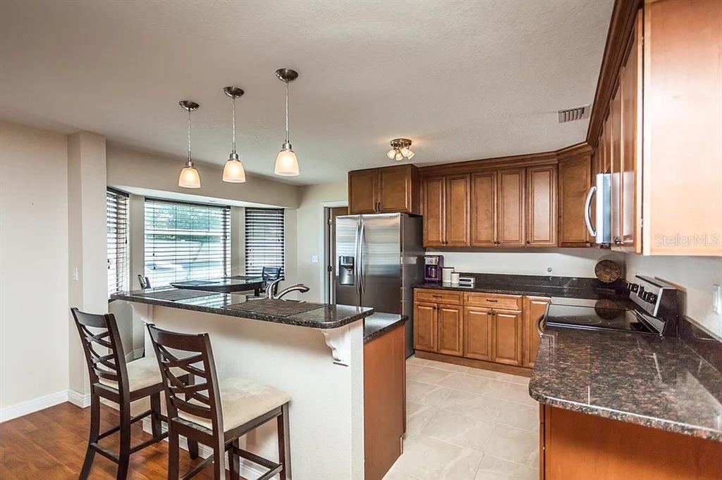 A kitchen features wood cabinets, granite countertops, a breakfast bar with stools, and pendant lighting — 13920 JAMAICA DRIVE, SEMINOLE, FL