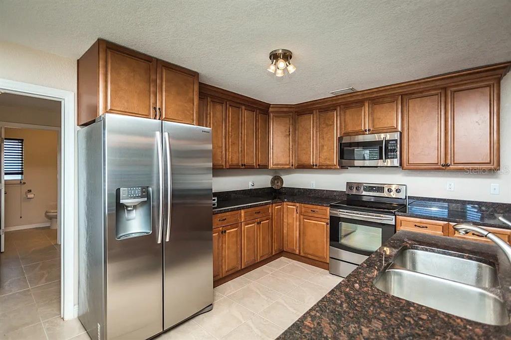A kitchen with wood cabinets, stainless steel appliances, and dark granite countertops — 13920 JAMAICA DRIVE, SEMINOLE, FL