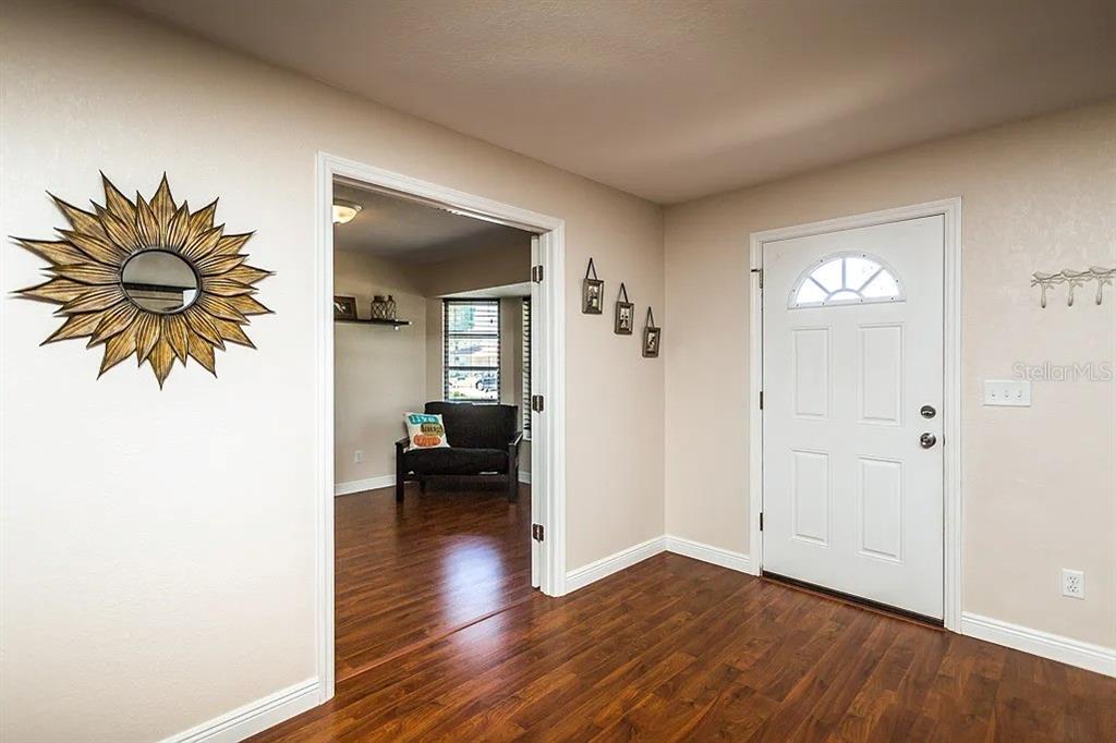 An entryway with wood-look flooring, a white front door, and a doorway leading to a room — 13920 JAMAICA DRIVE, SEMINOLE, FL