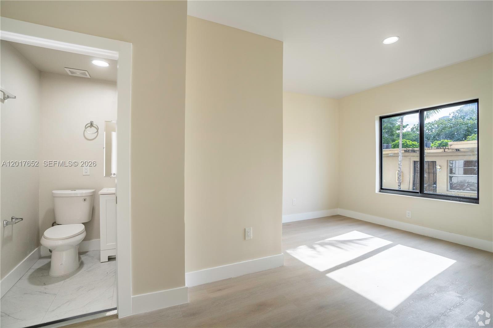 A bedroom with light-colored walls and wood-look flooring features an attached bathroom with tile — 433 SW 6th St # 10, Miami FL 33130, MIAMI, FL