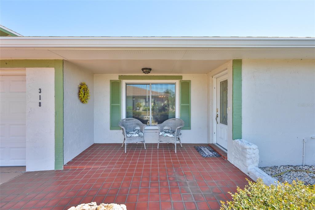 The exterior of a house features a tiled porch, two wicker chairs, and green shutters — 318 FAIRSIDE COURT, SUN CITY CENTER, FL