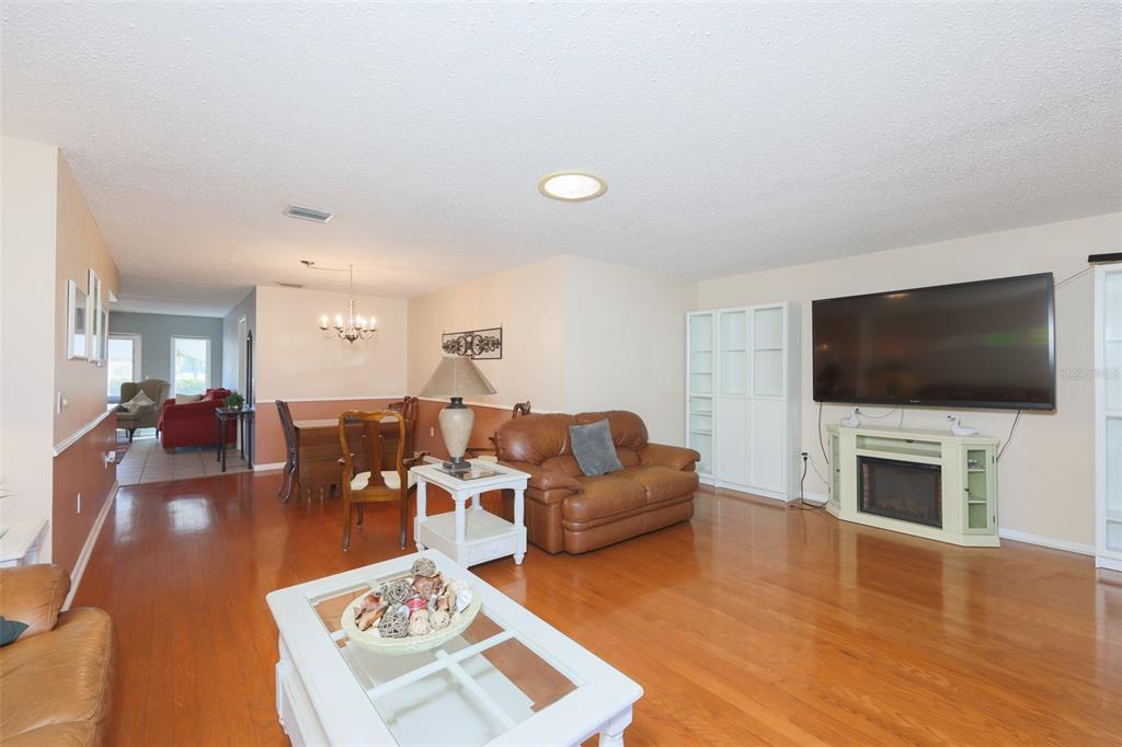 A living room with hardwood floors, a brown leather sofa, and a wall-mounted television — 318 FAIRSIDE COURT, SUN CITY CENTER, FL