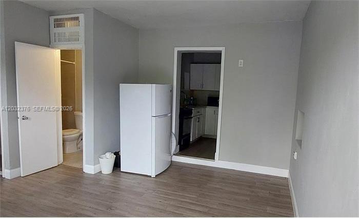 A room with light gray walls, wood-look flooring, a white refrigerator, and a bathroom doorway — 3735 NW 21st Ct # 3735, Miami FL 33142, MIAMI, FL