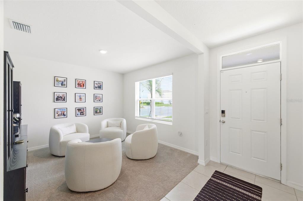 A bright entryway area features a carpeted seating space with three white chairs and photos — 8210 DOLPHIN BLUFF BOULEVARD, WESLEY CHAPEL, FL