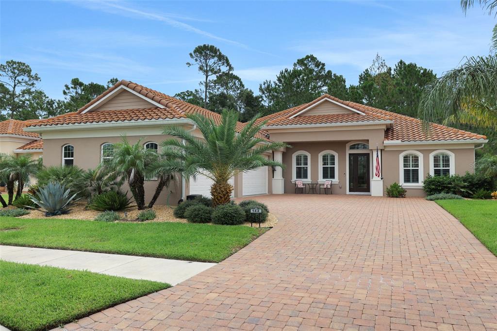 A single-story house with a terracotta tile roof, beige stucco walls, and a brick driveway — 142 PORTOFINO BLVD, NEW SMYRNA BEACH, FL