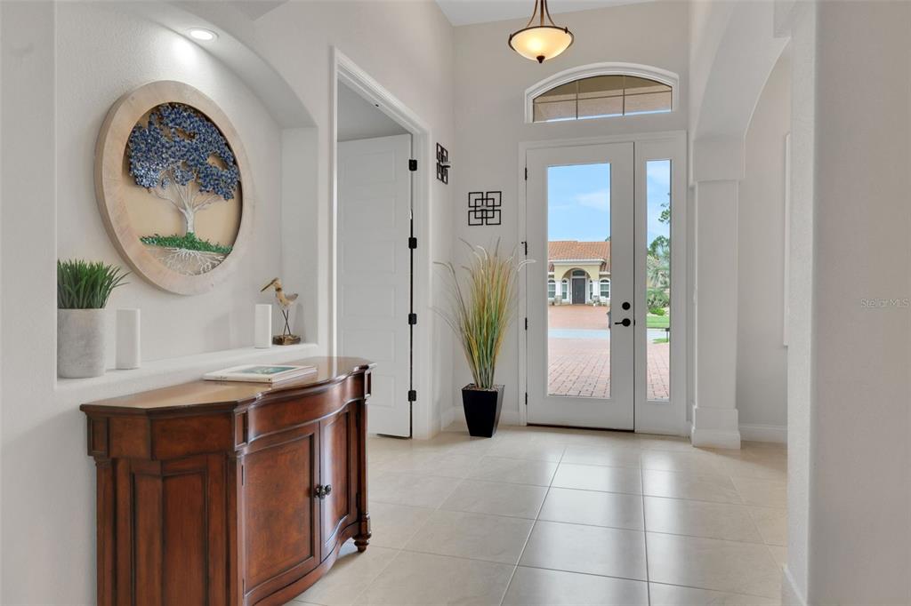A bright entryway features tile flooring, a wooden console table, and a circular wall art piece — 142 PORTOFINO BLVD, NEW SMYRNA BEACH, FL