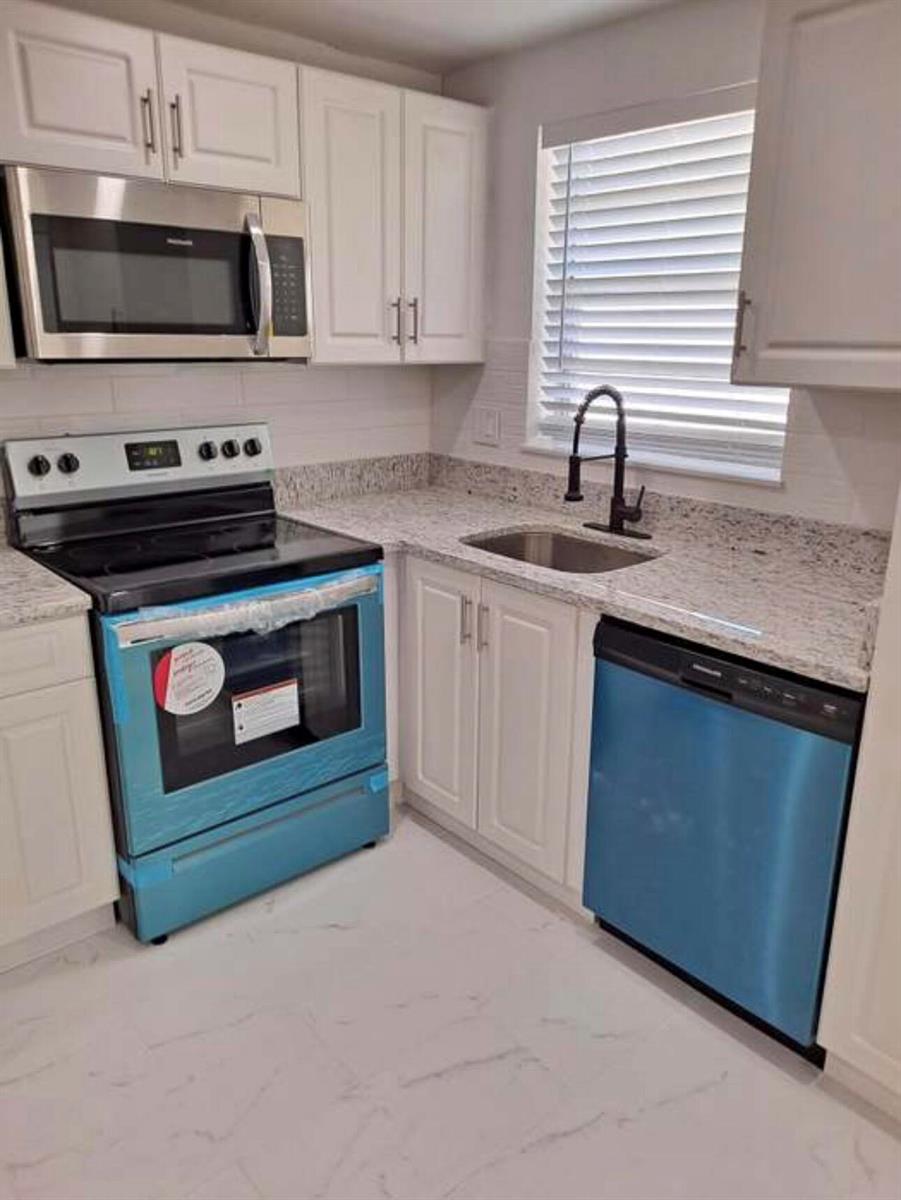 A kitchen features white cabinets, granite countertops, stainless steel appliances, and a black faucet — 603 S State Road 7 # 2i, Margate FL 33068, MARGATE, FL