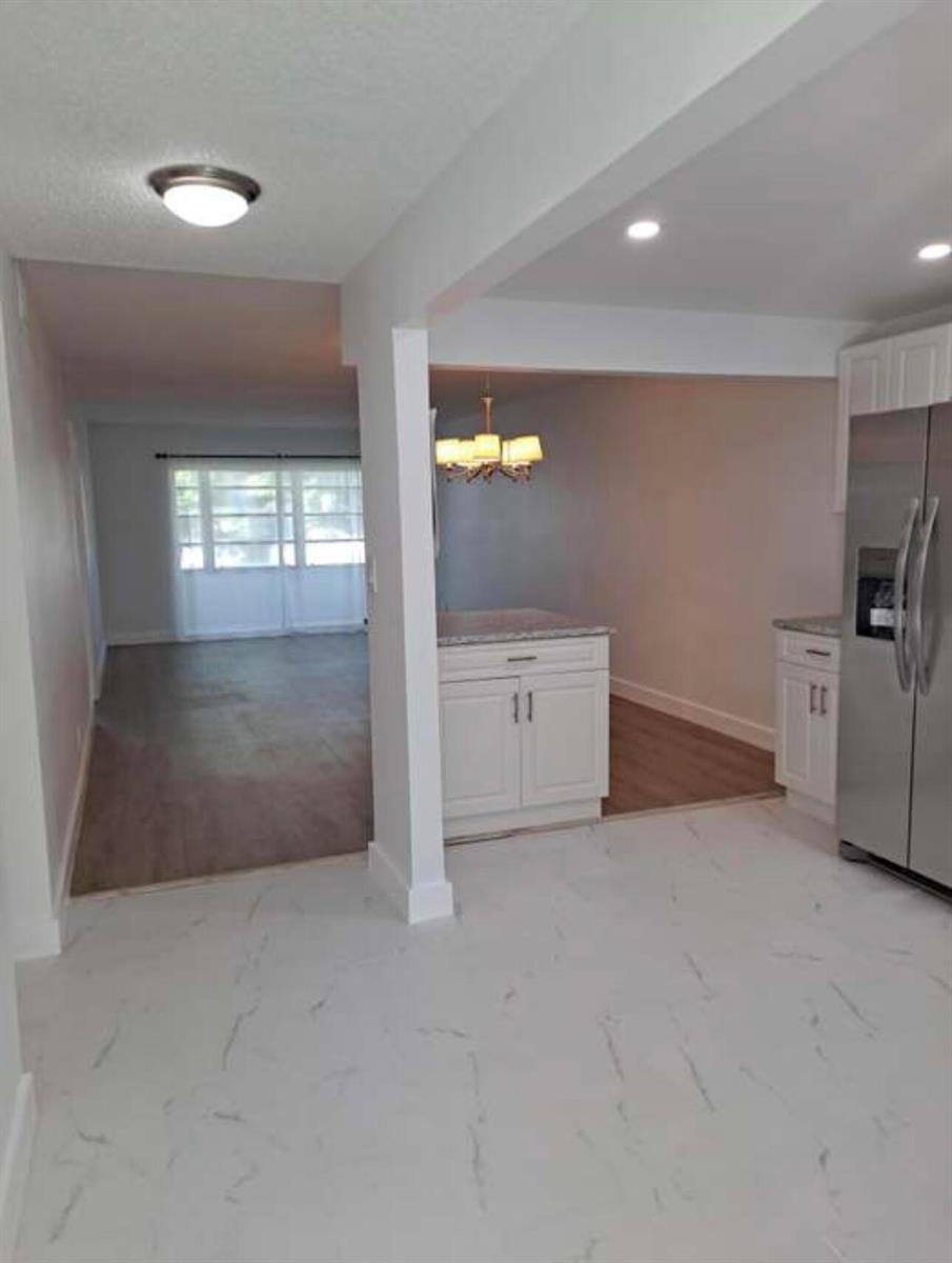 A kitchen with white cabinets and marble-look tile flooring opens into a living area — 603 S State Road 7 # 2i, Margate FL 33068, MARGATE, FL