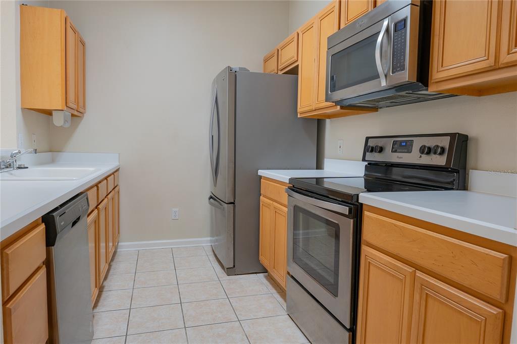 A kitchen features light wood cabinets, stainless steel appliances, white countertops, and tiled flooring — 13524 TURTLE MARSH LOOP UNIT 623, ORLANDO, FL