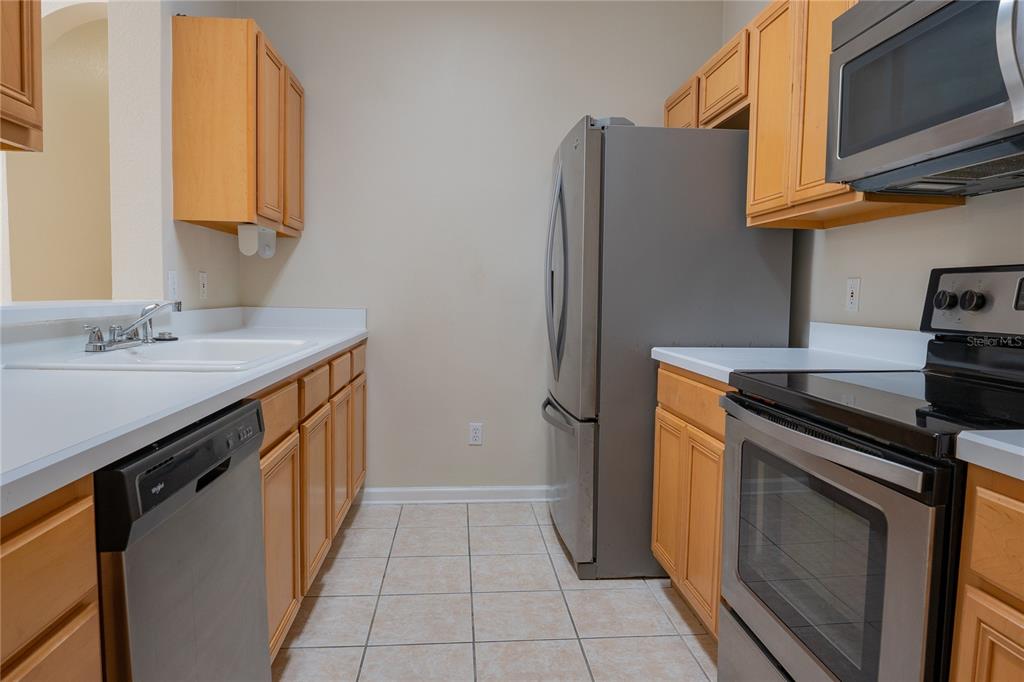 A kitchen features light wood cabinets, white countertops, and stainless steel appliances on tiled floors — 13524 TURTLE MARSH LOOP UNIT 623, ORLANDO, FL
