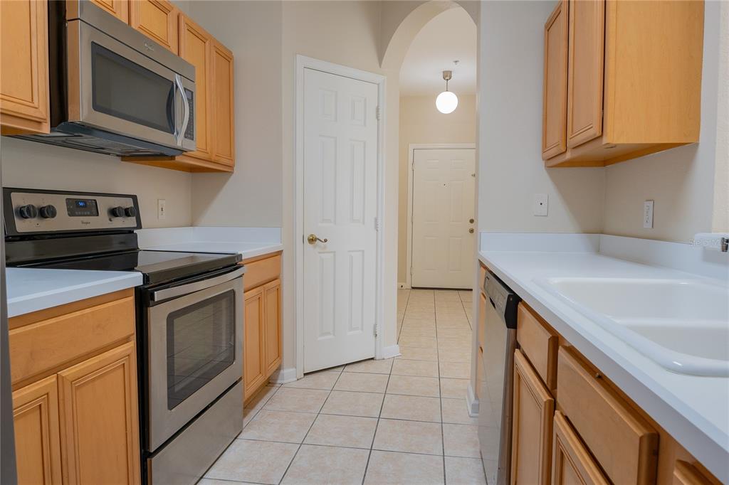 A galley kitchen features light wood cabinets, stainless steel appliances, and white tile flooring — 13524 TURTLE MARSH LOOP UNIT 623, ORLANDO, FL