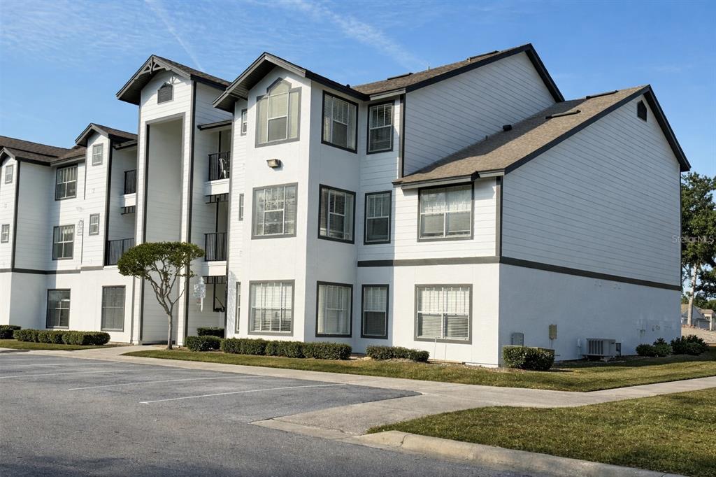 A three-story apartment building with white siding, dark trim, and a parking lot in front — 2201 KEY WEST COURT UNIT 328, KISSIMMEE, FL