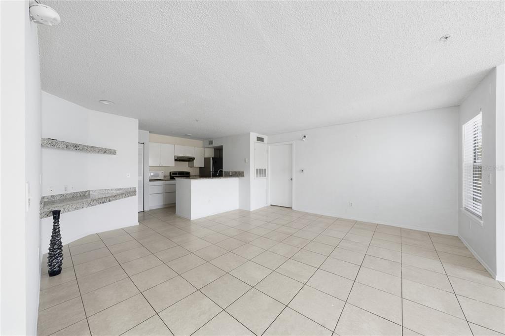 An open-concept living area features white walls, light-colored tile flooring, and a kitchen with granite countertops — 2201 KEY WEST COURT UNIT 328, KISSIMMEE, FL