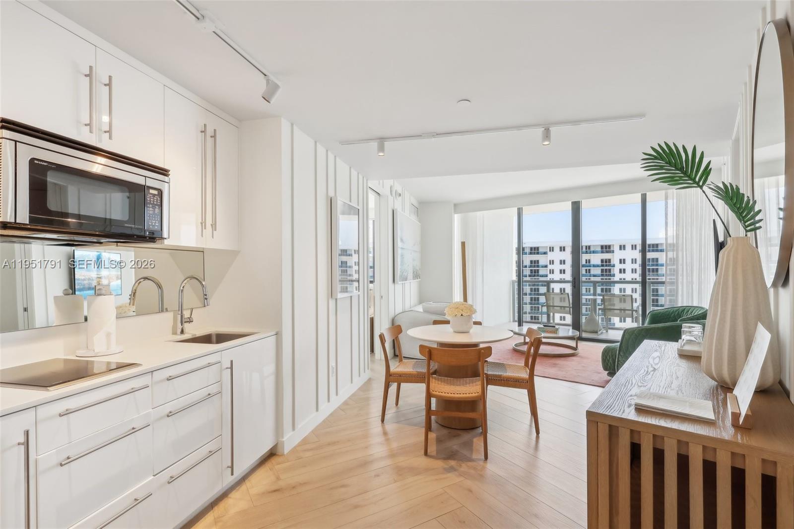 A modern kitchen and dining area feature white cabinetry, light wood flooring, and balcony views — 2201 Collins Ave # 1511, Miami Beach FL 33139, MIAMI BEACH, FL