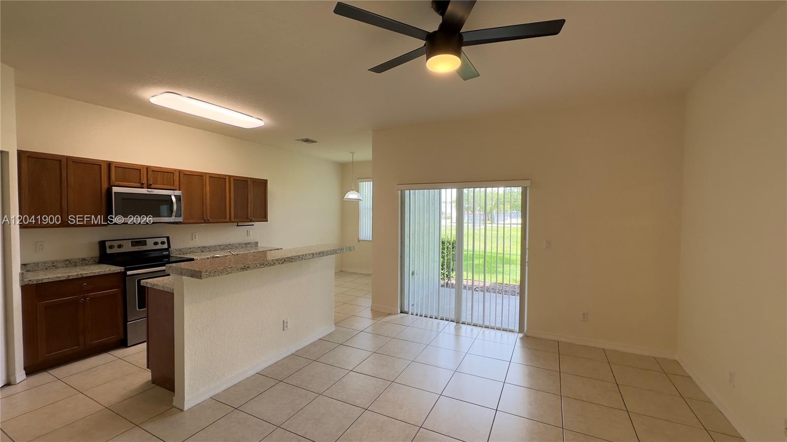 A kitchen with brown cabinets and granite countertops opens into a tiled dining area — 3042 Grandiflora Dr, Green Acres FL 33467, GREEN ACRES, FL